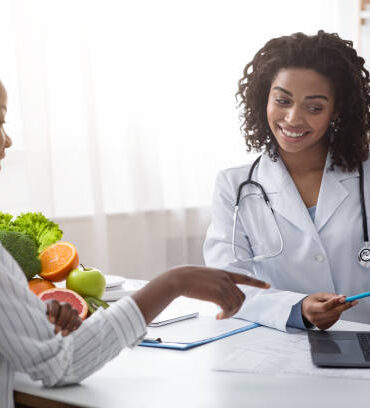 Personal nutrition plan. African american woman dietologist consulting patient, using laptop, clinic interior